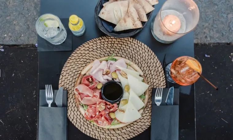 Tagliere di salumi e formaggi visto dall'alto, accanto a un bicchiere da aperitivo